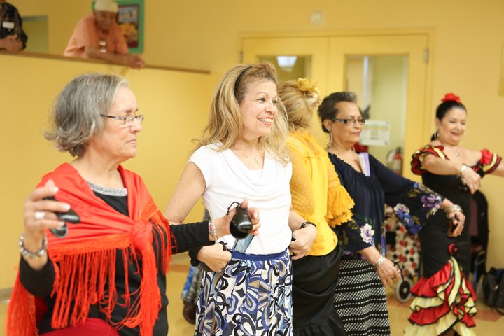 Photo of a group of women, dressed for Flamenco dancing, wearing shawls and holding musical instruments.